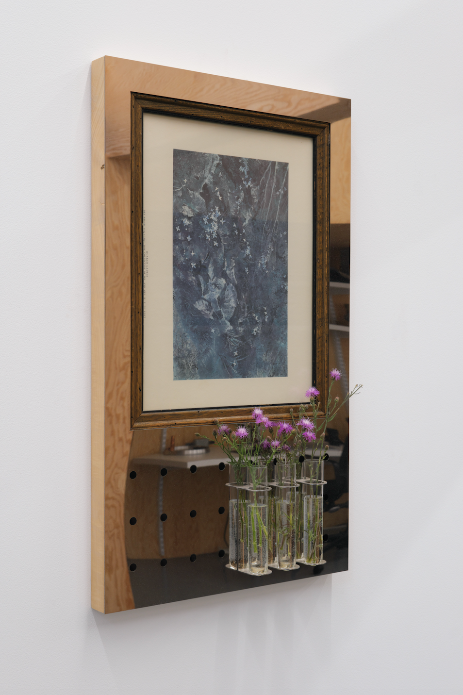 Wooden-framed mirror with a floral arrangement on a white wall