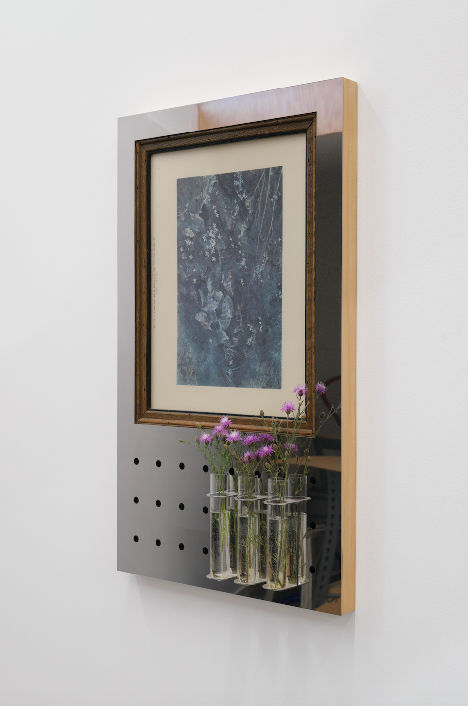 Framed artwork with a metallic panel and floral arrangement on a white wall with vintage print