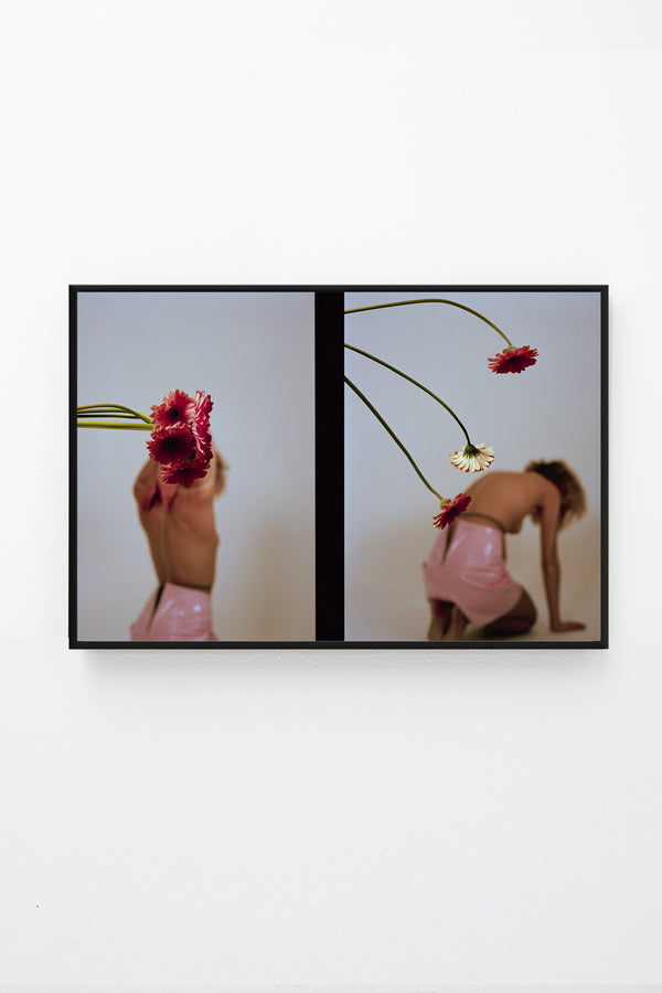 2 images of topless woman and Gerber daisies, framed on wall.