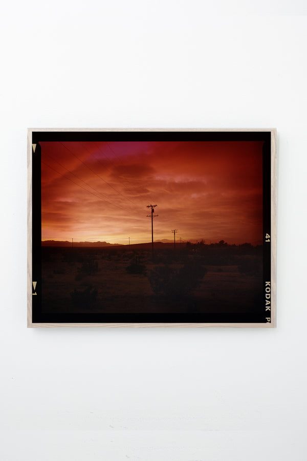 Red sky over desert landscape with telephone poles, framed on white wall.