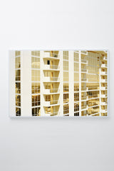 Mirrored windows of apartment building reflect gold light, framed.