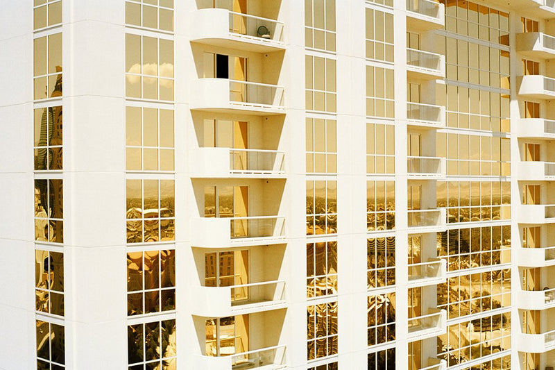 Mirrored windows of apartment building reflect gold light, unframed.