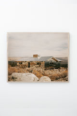 House made of mirrors in a rocky, mountainous landscape, framed on white wall.