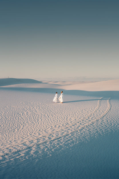 Two people stand in a desert scape, tire tracks beside them.
