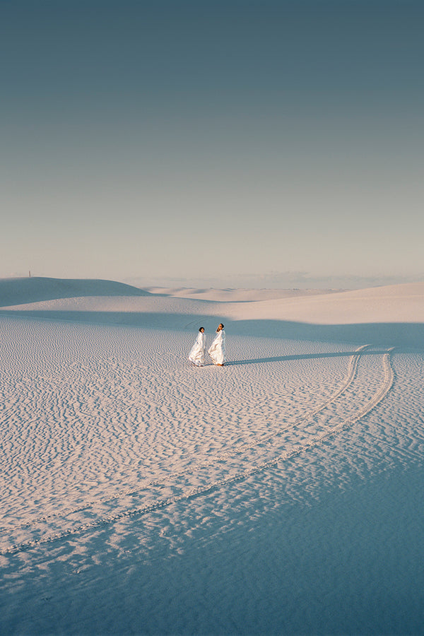 Two people stand in a desert scape, tire tracks beside them.