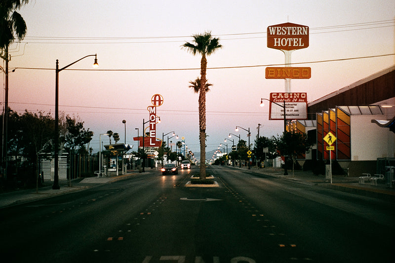 Street lined with casino and motel signs, cars, and palm trees.