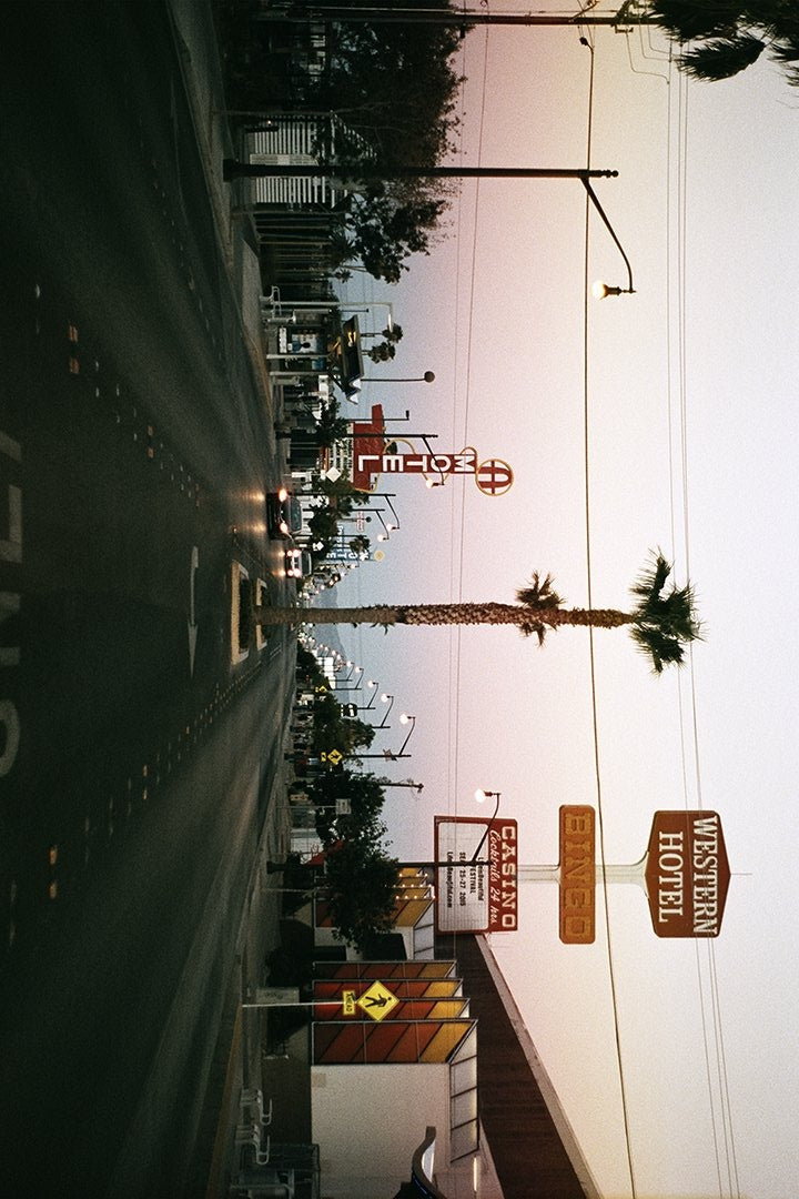 Street lined with casino and motel signs, cars, and palm trees.